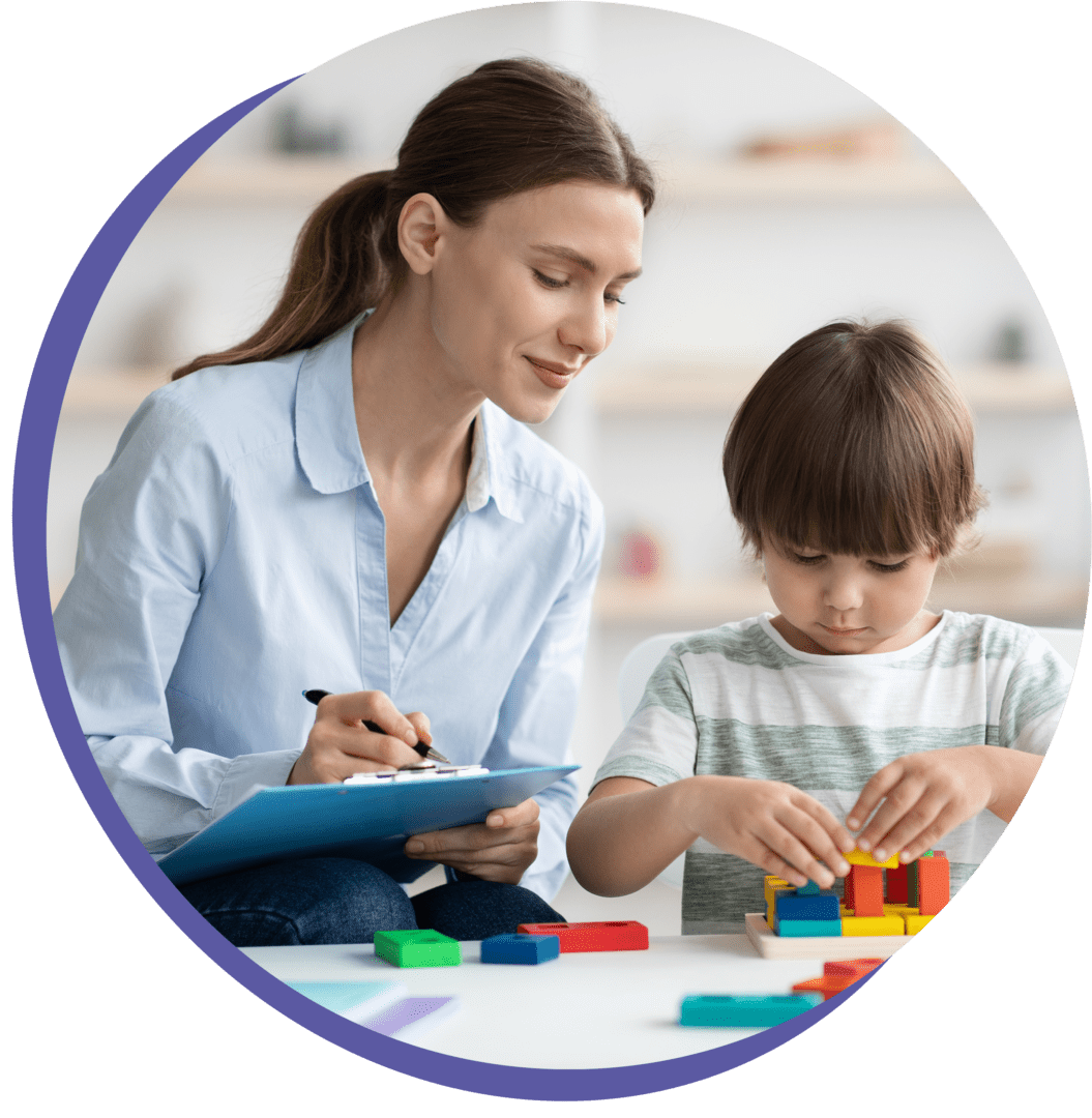 A woman observes and takes notes as a child concentrates on building a structure with colorful blocks.